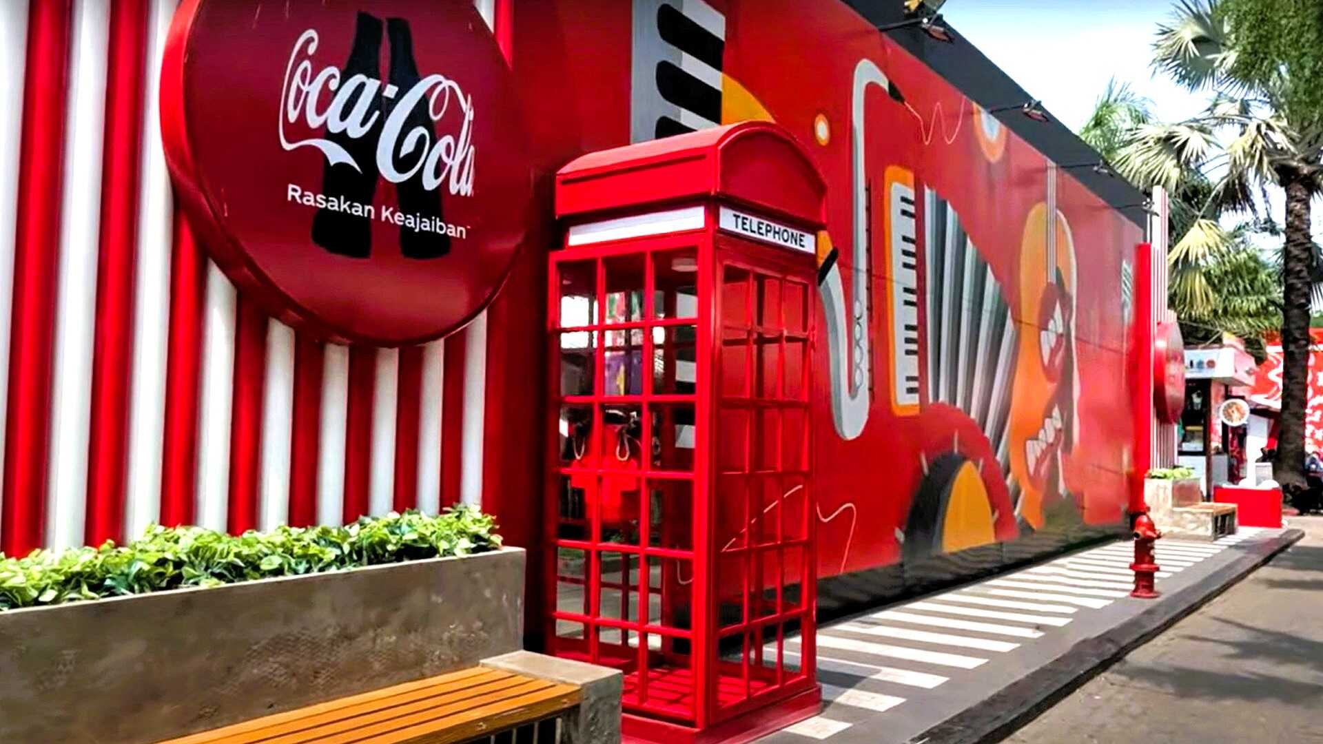 A red telephone booth next to a red building that showcases a musical mural with Coca-Cola branding.