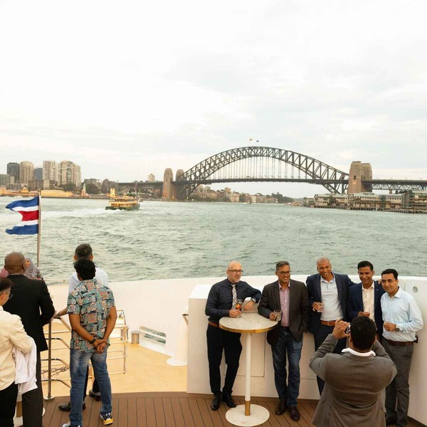 Ericsson-End-Of-Year-Celebrations-PMG-3.jpg A lively group of Ericsson guests gathered on a boat's deck, sharing laughter and conversation against a backdrop of the Sydney Harbour Bridge.