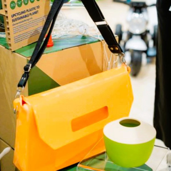 A yellow ladies' bag refashioned from rubber gloves rests on a table beside a green and white vessel, creating a vibrant and stylish arrangement.