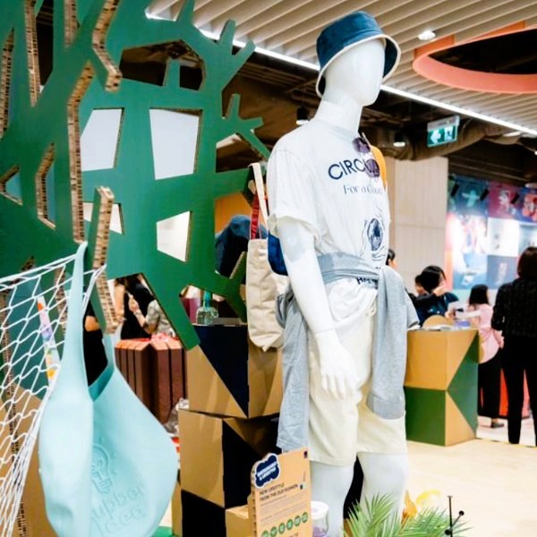A mannequin in eco-friendly apparel with a hat and a bag stands in front of a retail display.