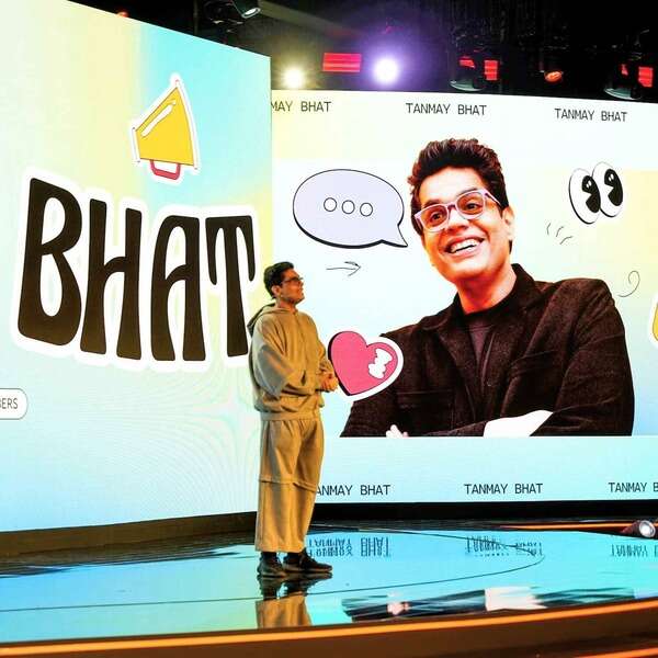 YouTube-Brandcast-2024-India-PMG-4.jpg Tanmay Bhat speaking on stage, standing beside a large screen that displays a cheerful image of him.